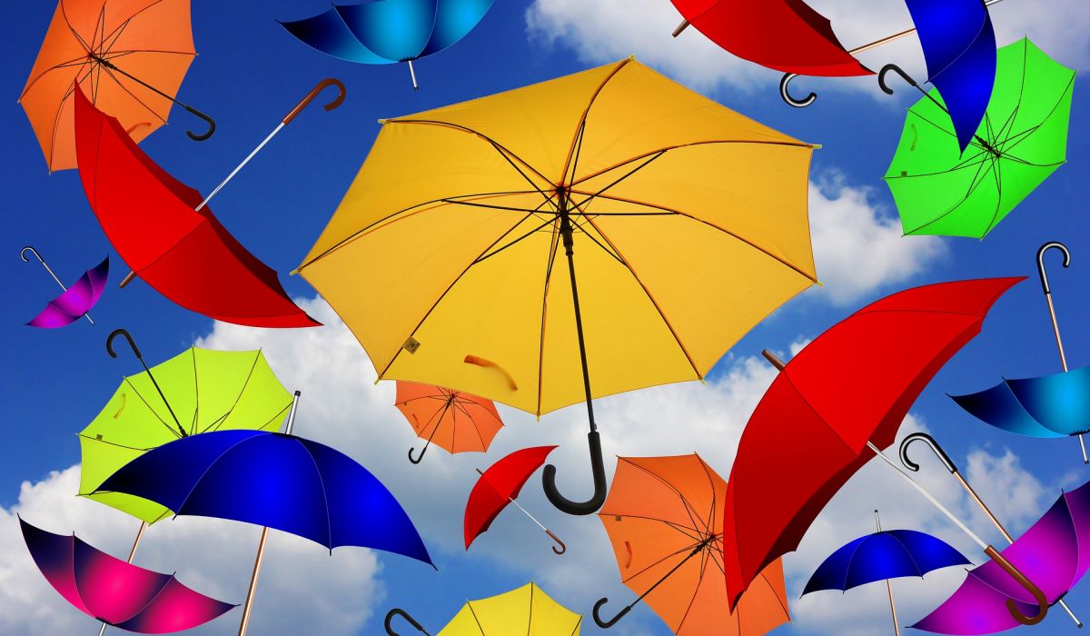 Parapluies de toutes les couleurs flottant, ouverts, dans un ciel d'un bleu intense et nuageux